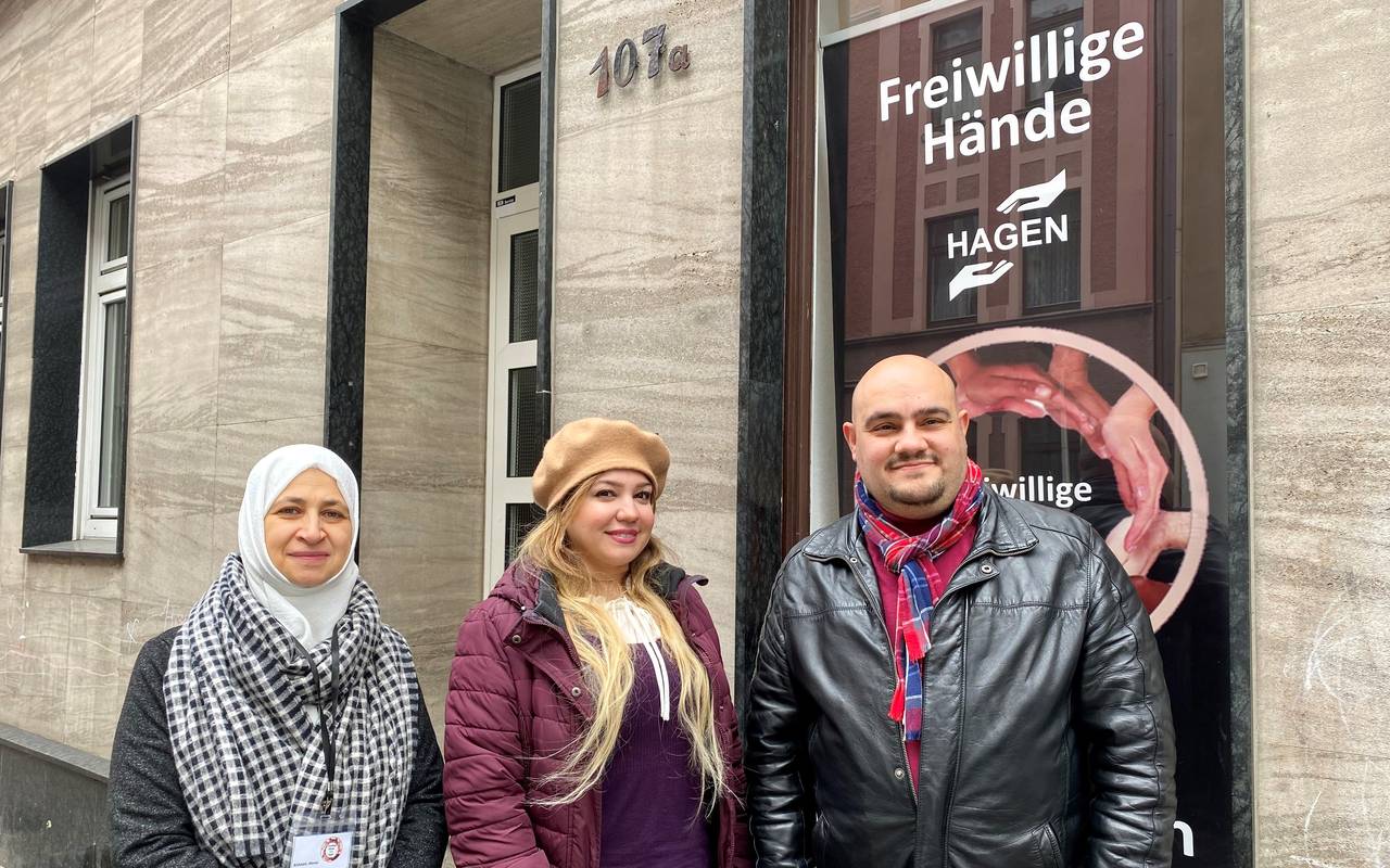 Ahmad Alali und zwei weibliche Mitglieder des Vereins stehen vor dem Vereinssitz der "Freiwilligen Hände". Hinter ihnen sieht man im Fenster den Banner des Vereins.