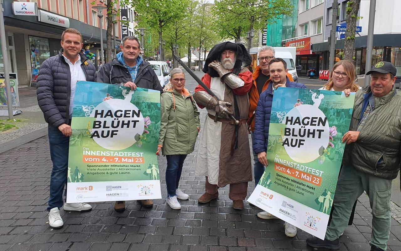 Mehrere Menschen stehen in einem Halbkreis. Sie halten Plakate in der Hand. Darauf steht: Hagen blüht auf.