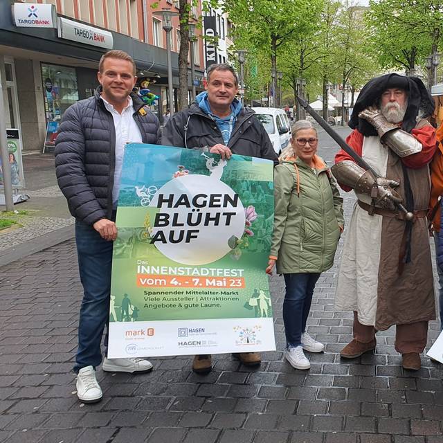 Mehrere Menschen stehen in einem Halbkreis. Sie halten Plakate in der Hand. Darauf steht: Hagen blüht auf.