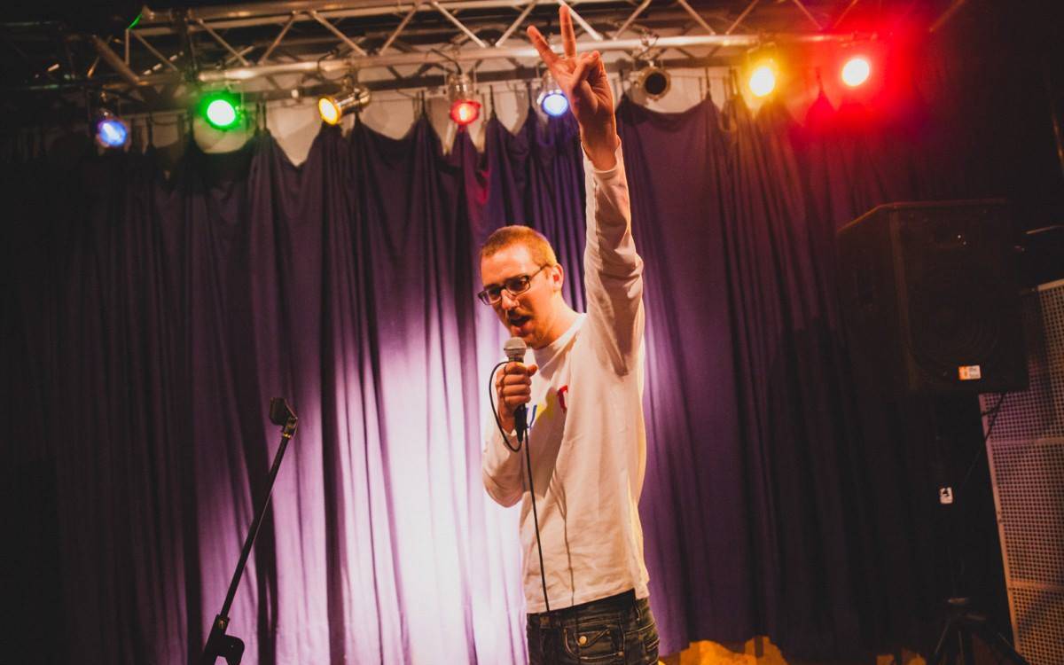 Man sieht Jan Schmidt auf einer Bühne einen Poetry Slam performen. Er organisiert und moderiert den Dead or Alive Poetry Slam.