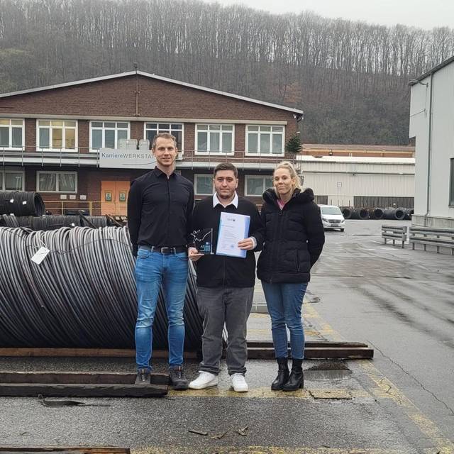 Zu sehen sind 3 Leute vor Stahldrähten bei den Deutschen Edelstahlwerken. Darunter der Ausbildungsleiter Kristian Baum, Vertreterin des Ausbildungsrates und der Azubi Bora Turan, der seinen Preis hält.