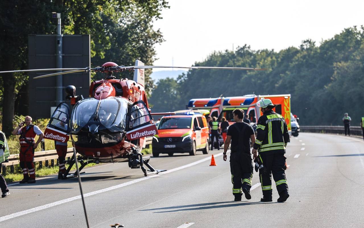 Ein roter Rettungshubschrauber steht auf der Straße. Neben ihm stehen zwei Feuerwehrleute. Im Hintergrund sieht man mehrere Rettungsfahrzeuge.