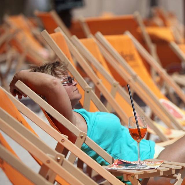 Eine Frau genießt mit einem Drink auf einem Liegestuhl die Mittagssonne am Stadtstrand.. Foto: Daniel Karmann dpa/lby