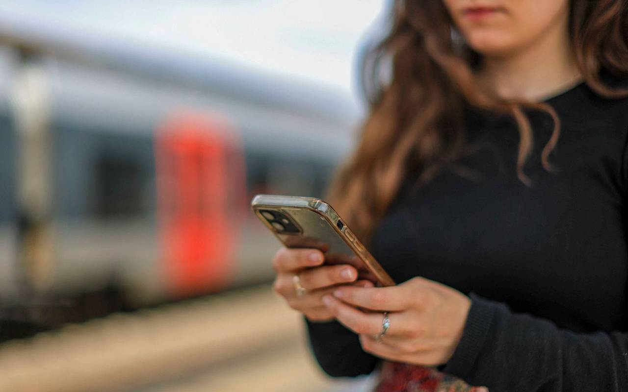 Eine junge Frau steht mit ihrem Mobiltelefon auf einem Bahnsteig