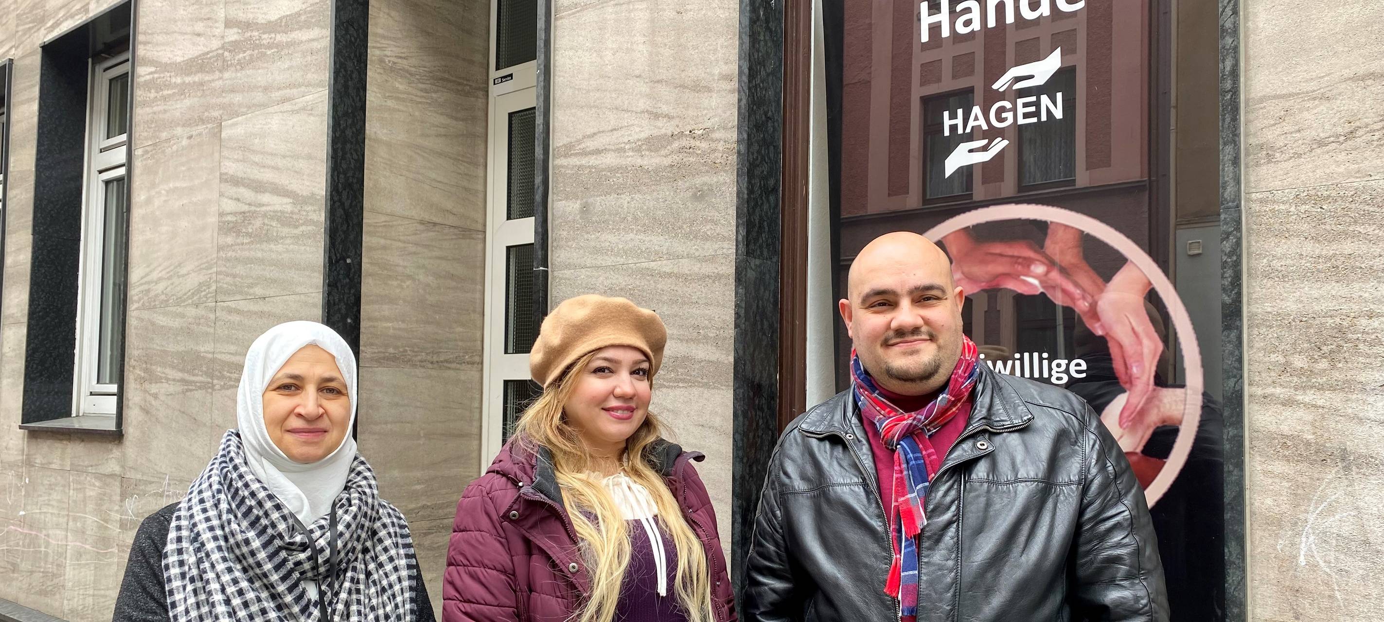 Ahmad Alali und zwei weibliche Mitglieder des Vereins stehen vor dem Vereinssitz der "Freiwilligen Hände". Hinter ihnen sieht man im Fenster den Banner des Vereins.