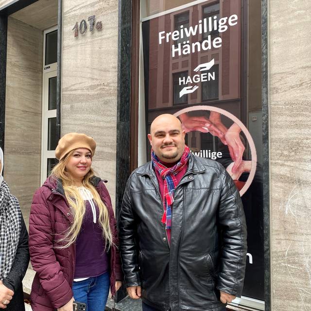 Ahmad Alali und zwei weibliche Mitglieder des Vereins stehen vor dem Vereinssitz der "Freiwilligen Hände". Hinter ihnen sieht man im Fenster den Banner des Vereins.