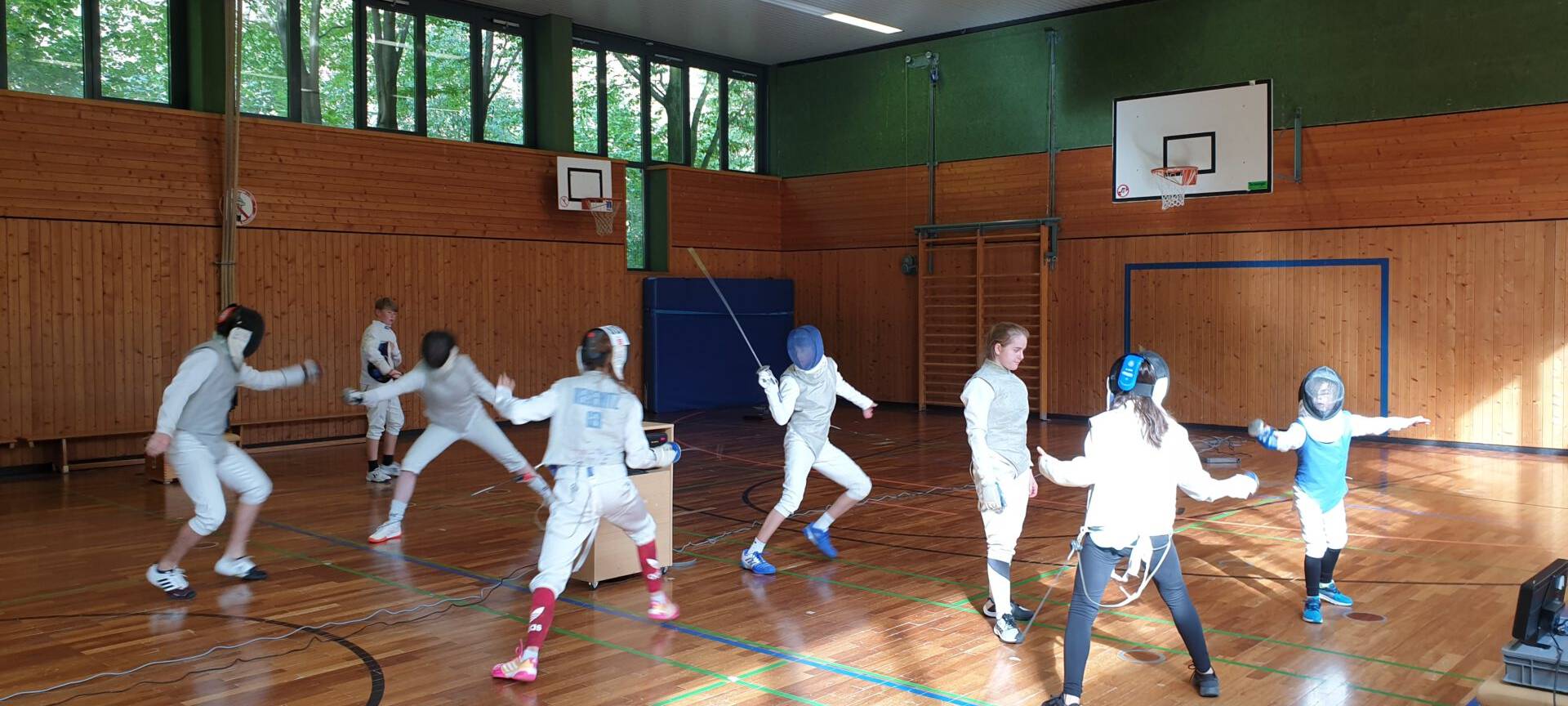 Kinder in Fechtkleidung kämpfen im Zweikampf. Sie sind in einer Turnhalle.