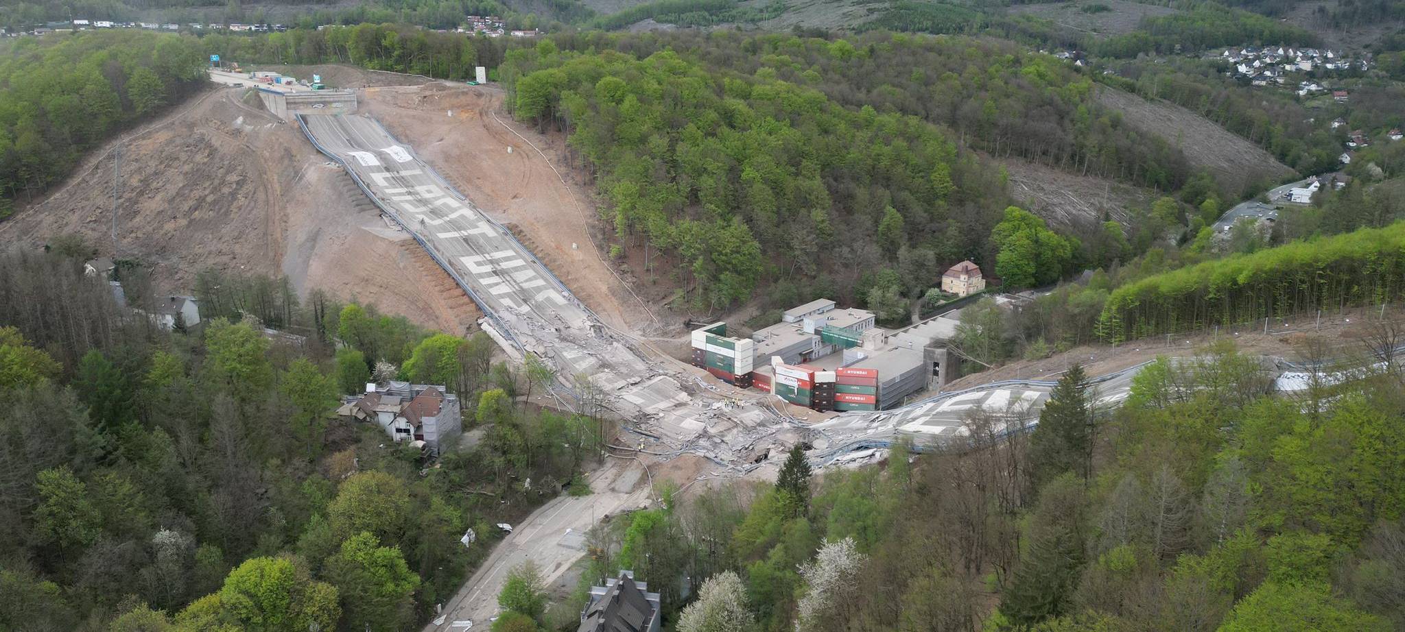 Gesprengte Brücke. Brückenteile liegen auf der Erde. Auf den Teilen steht der Spruch "Lasst uns Brücken bauen".