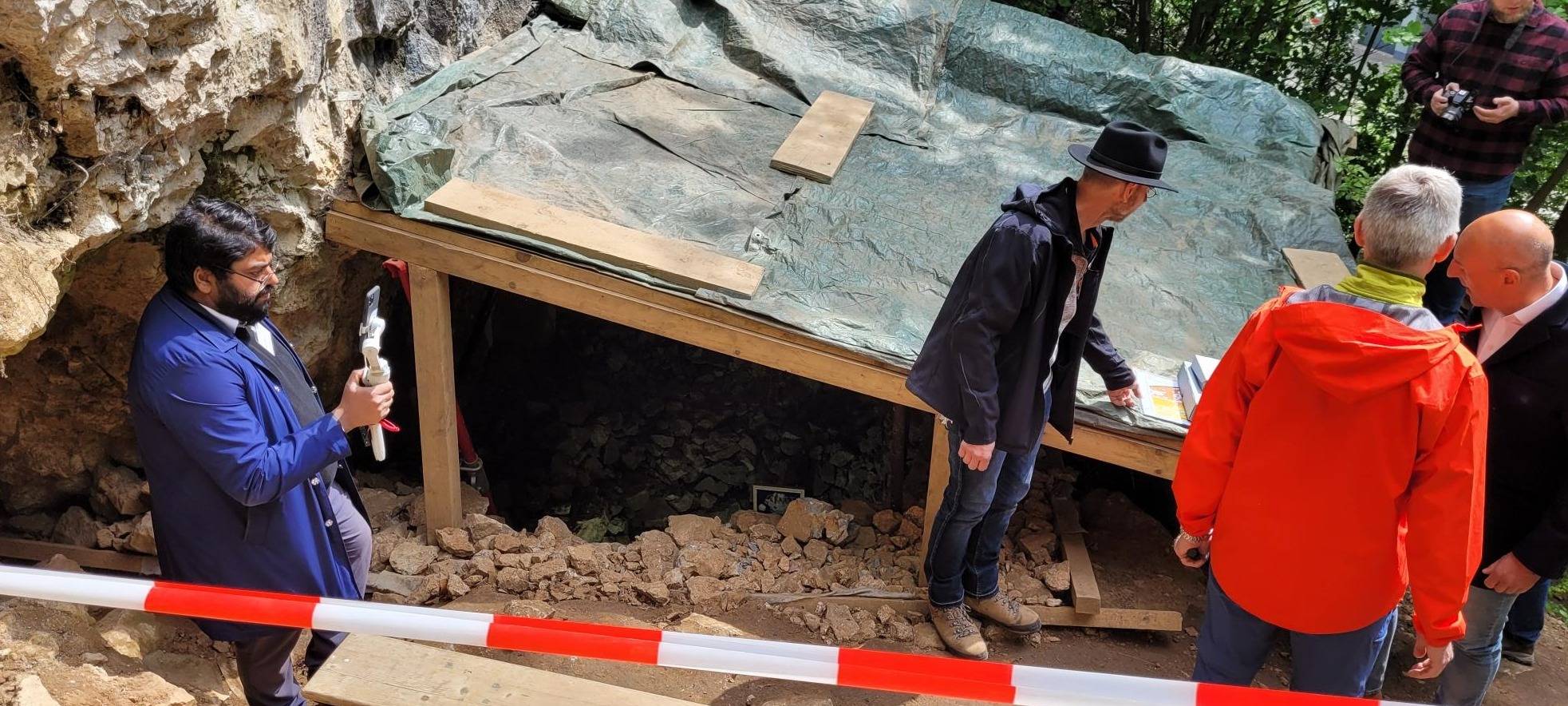 Zu sehen sind Archäologen an der Blätterhöhle, auf einer Plane sind zudem Pläne sowie die archäologischen Funde aus der Höhle zu sehen.