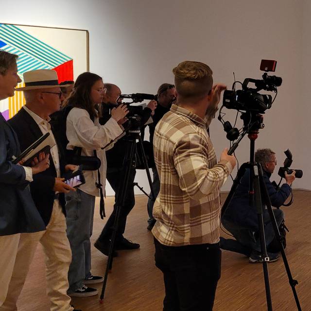 Zu sehen sind verschiedene Reporter, und Heinz Mack und Museumsdirektor Tayfun Belgin vor einem Gemälde Macks.