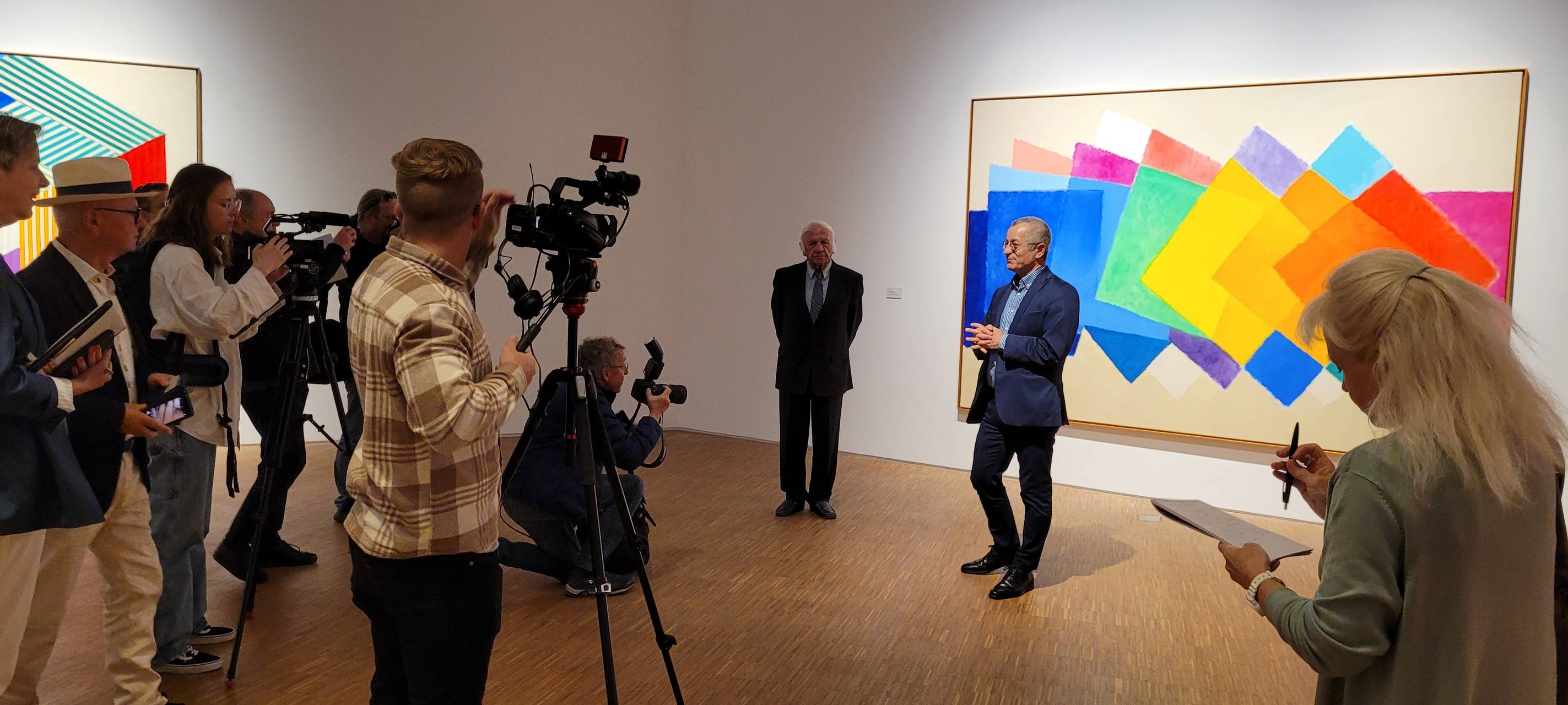 Zu sehen sind verschiedene Reporter, und Heinz Mack und Museumsdirektor Tayfun Belgin vor einem Gemälde Macks.