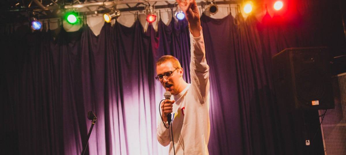 Man sieht Jan Schmidt auf einer Bühne einen Poetry Slam performen. Er organisiert und moderiert den Dead or Alive Poetry Slam.