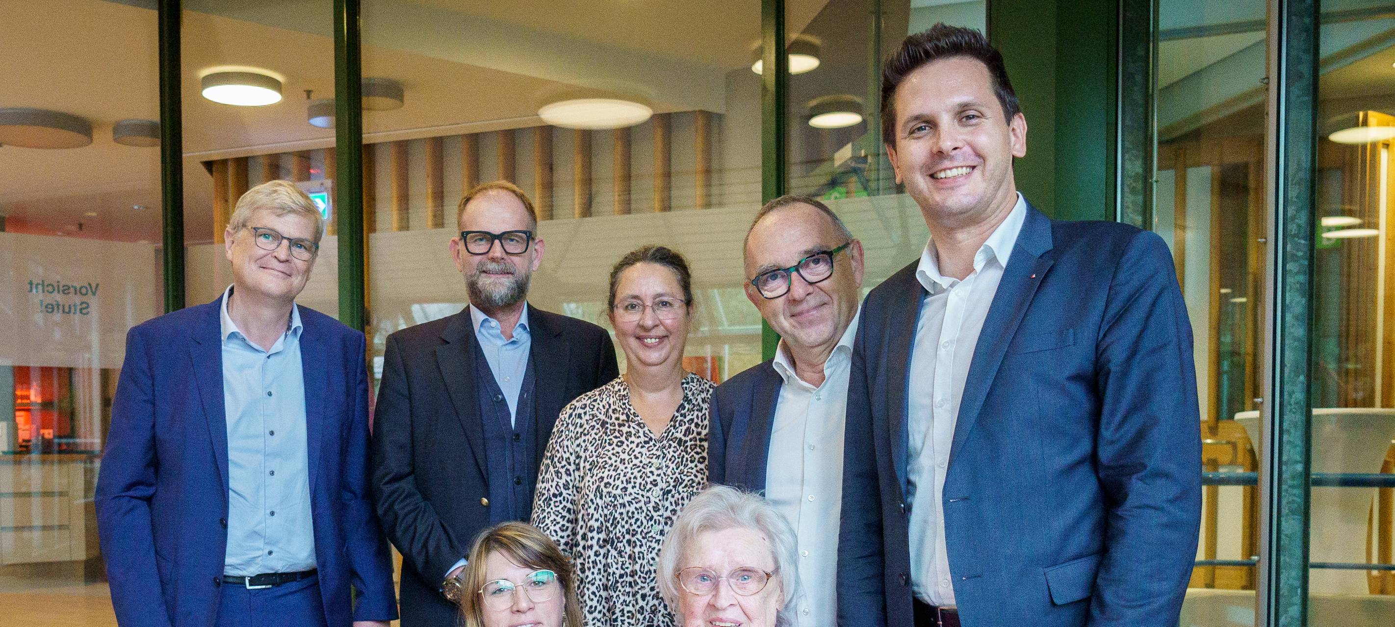 Mehrere Personen stehen hinter einem Tisch und gucken in die Kamera.