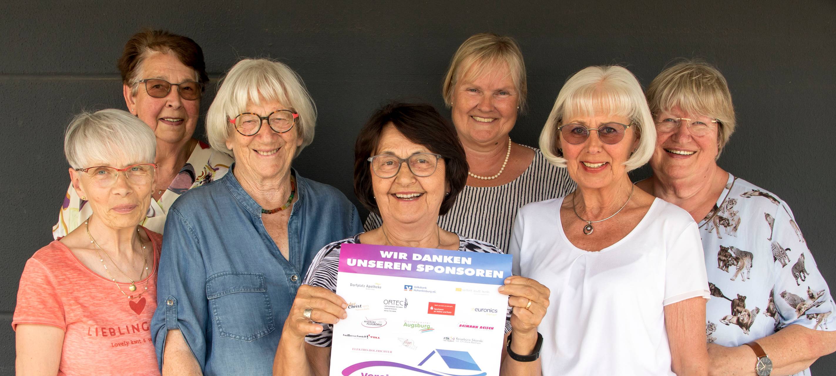 Sieben Frauen stehen in zwei Reihen und schauen in die Kamera