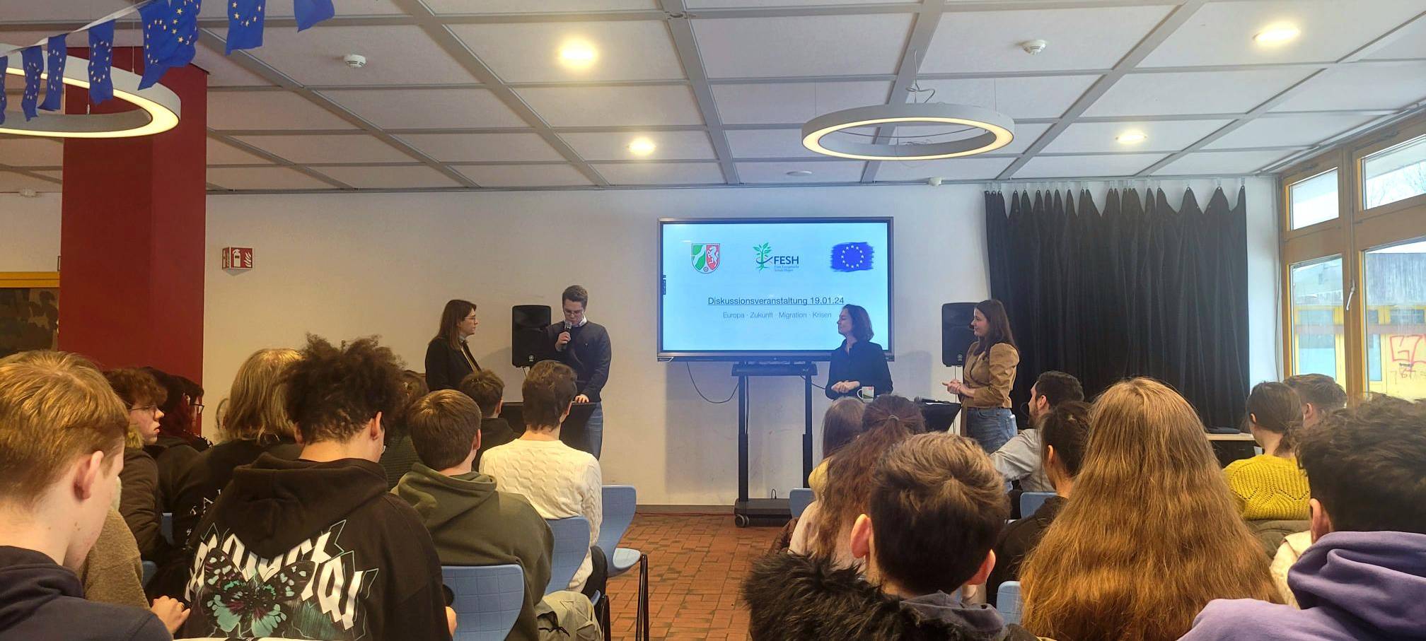 Man sieht Katarina Barley und Ina Blumenthal, die auf dem Podium in der Mensa der Gesamtschule Wehringhausen mit zwei Schülermoderatoren diskutieren