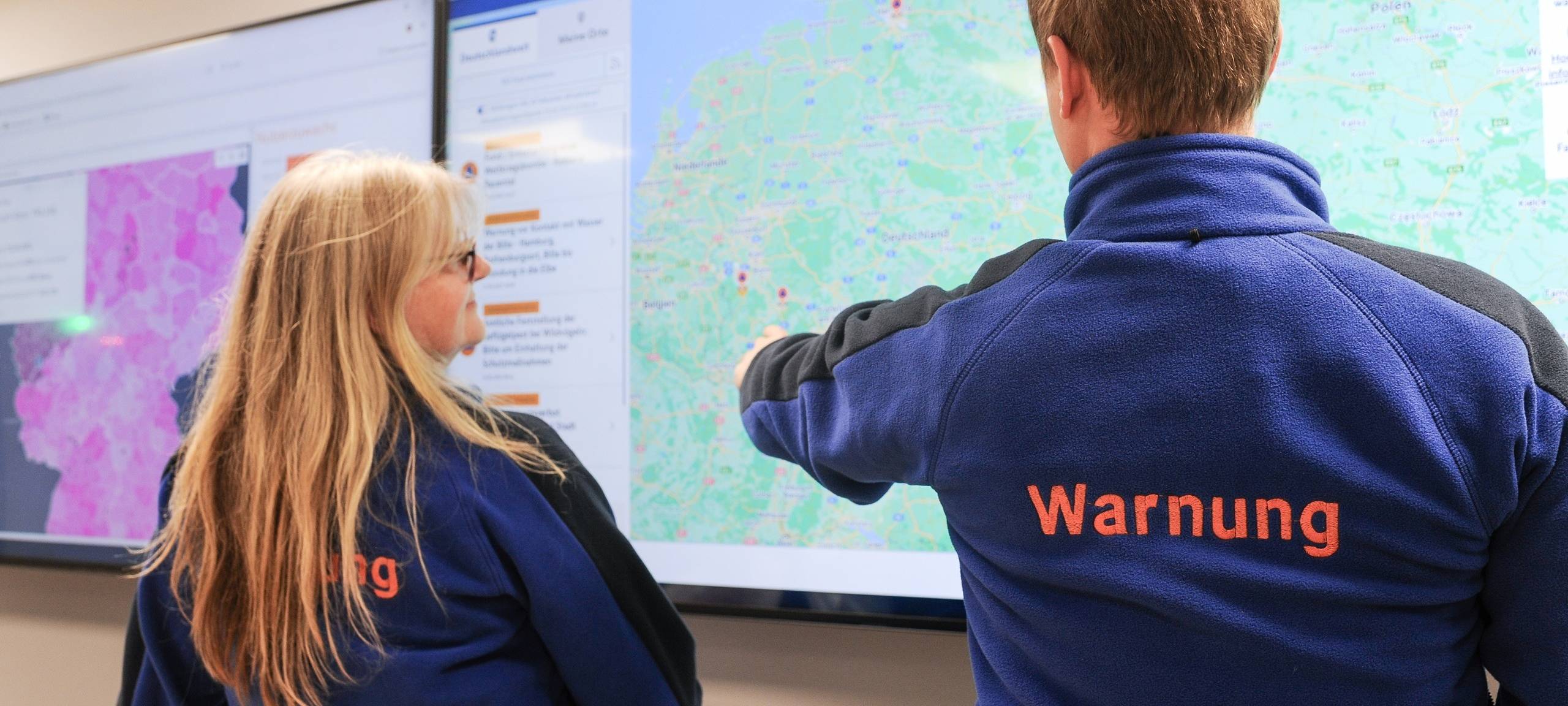 Zwei Personen stehen vor einem großen Bildschirm, der die Deutschland-Karte zeigt. Dies geschieht im Rahmen des bundesweiten Warntags.