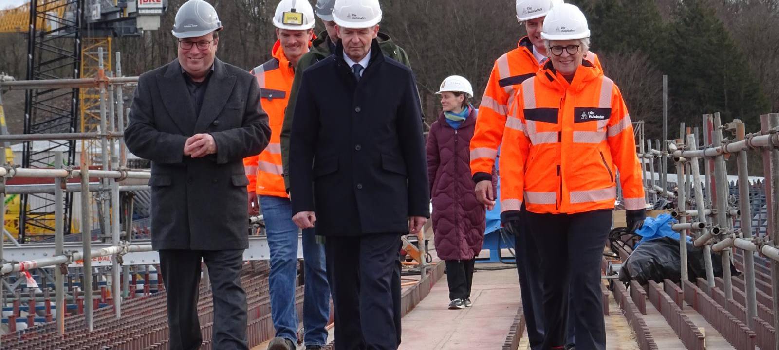 Mehrere Personen mit Bauhelmen stehen in der Nähe einer Brücke und schauen auf
