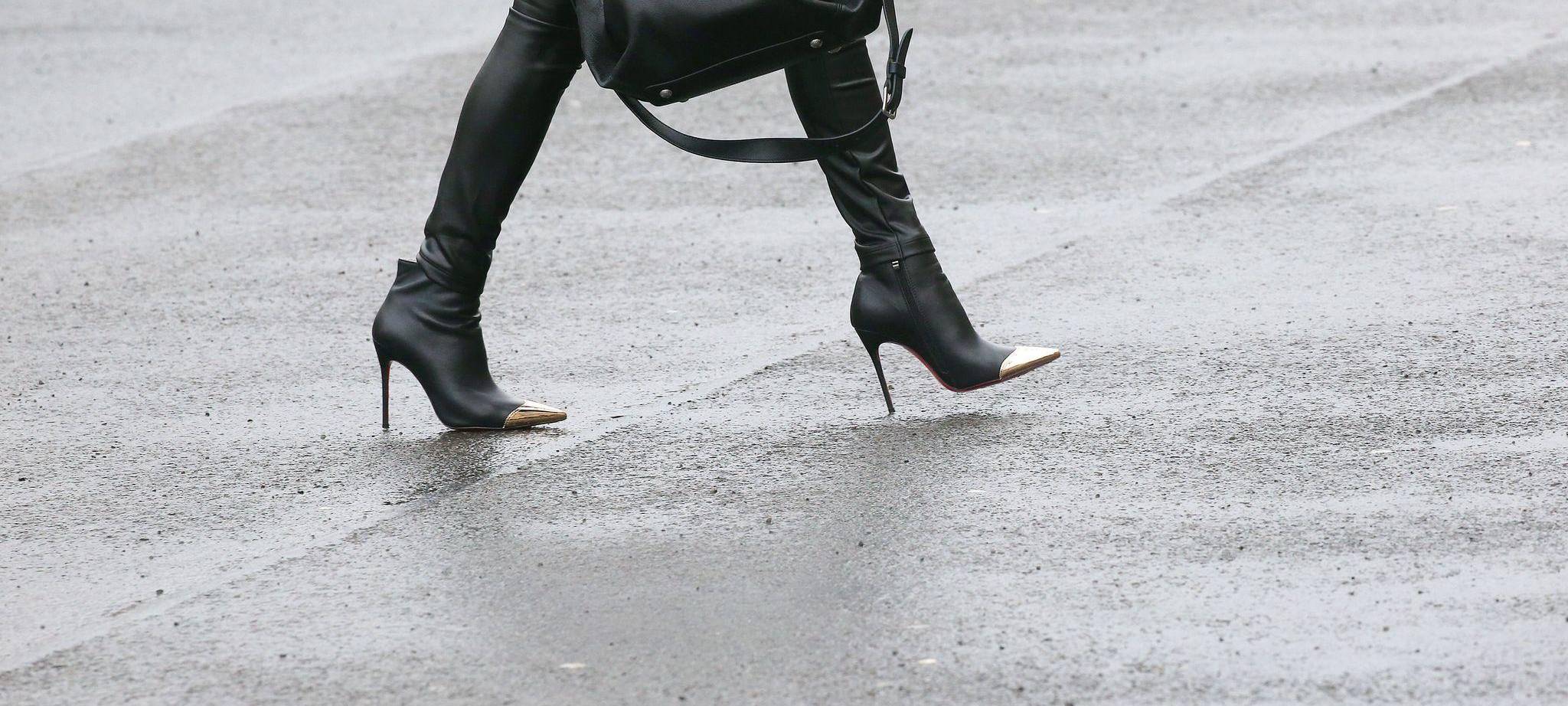 Frau mit High Heels geht über eine regennasse Straße