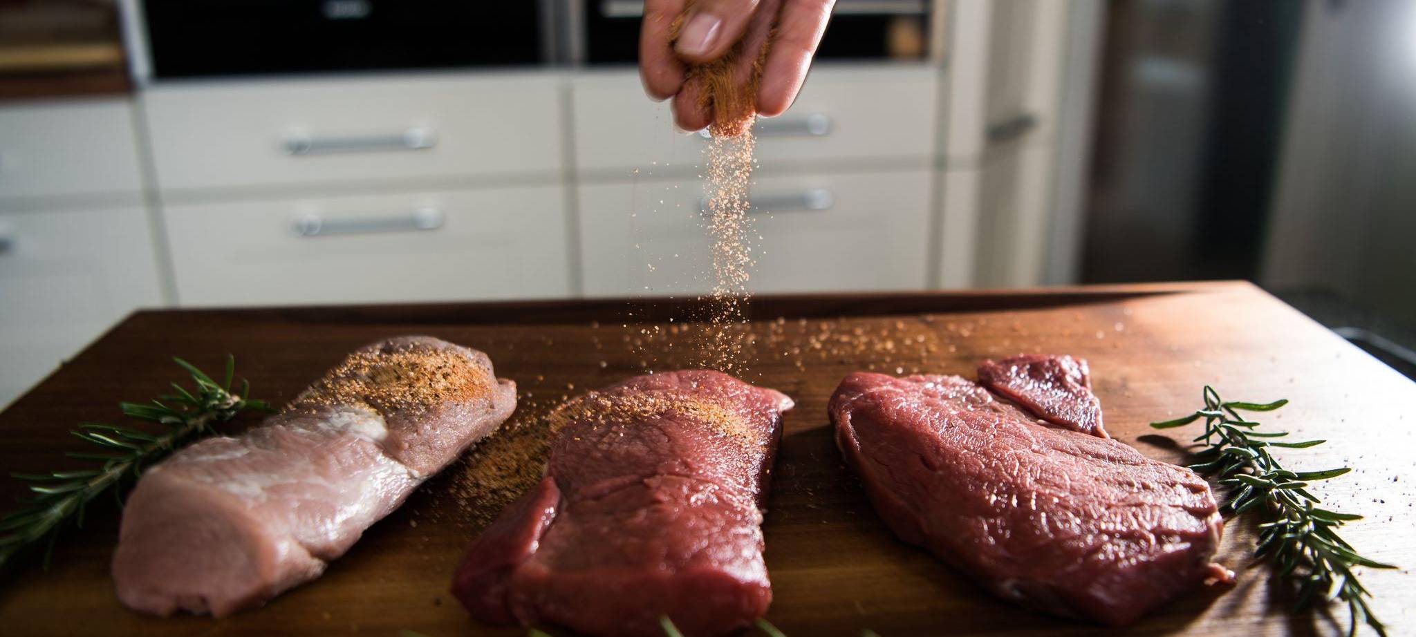 Eine Perosn würzt Fleisch