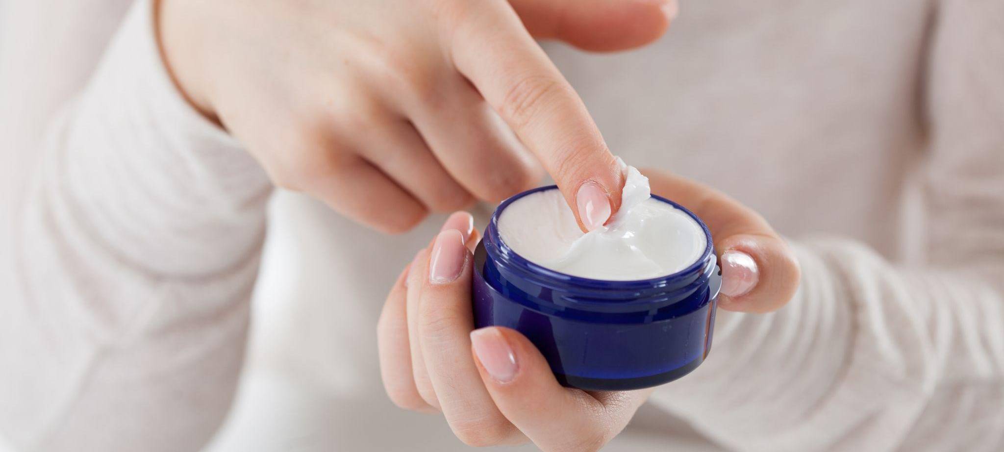 Eine Frau streicht mit dem Finger durch eine Cremedose