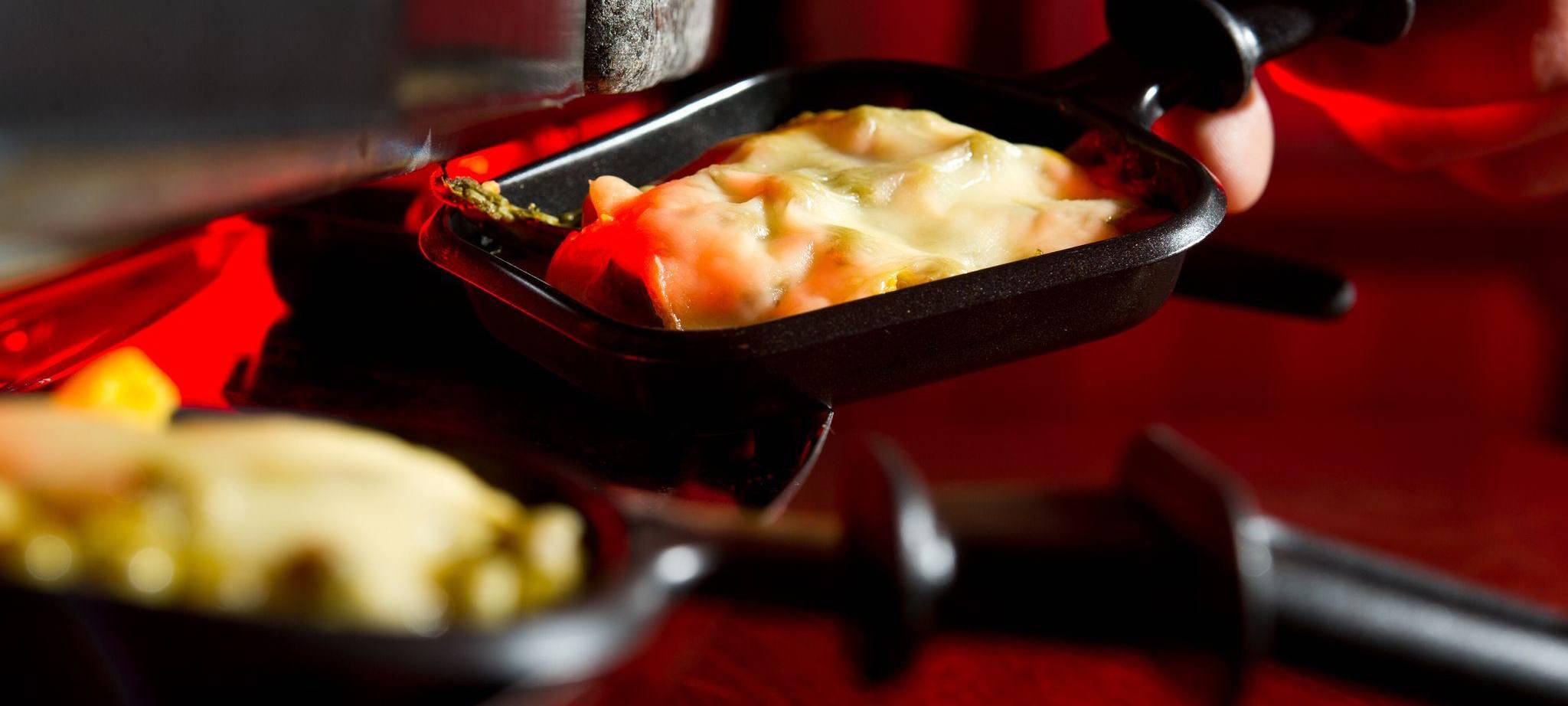 Mann hält ein Raclette-Pfännchen in der Hand