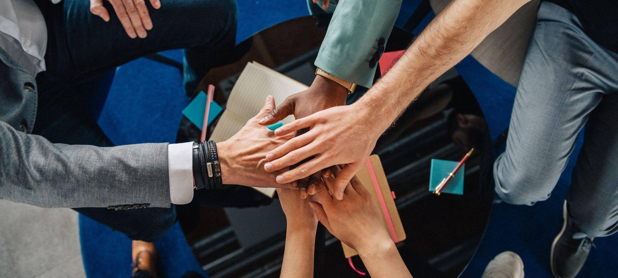 Gruppe Kolleginnen und Kollegen legen die Hände aufeinander