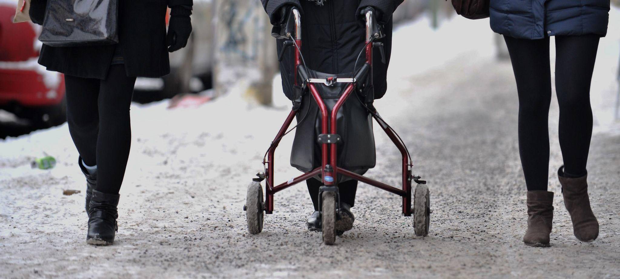 Ein Frau geht mit Rollator auf einem schneebedeckten Gehweg