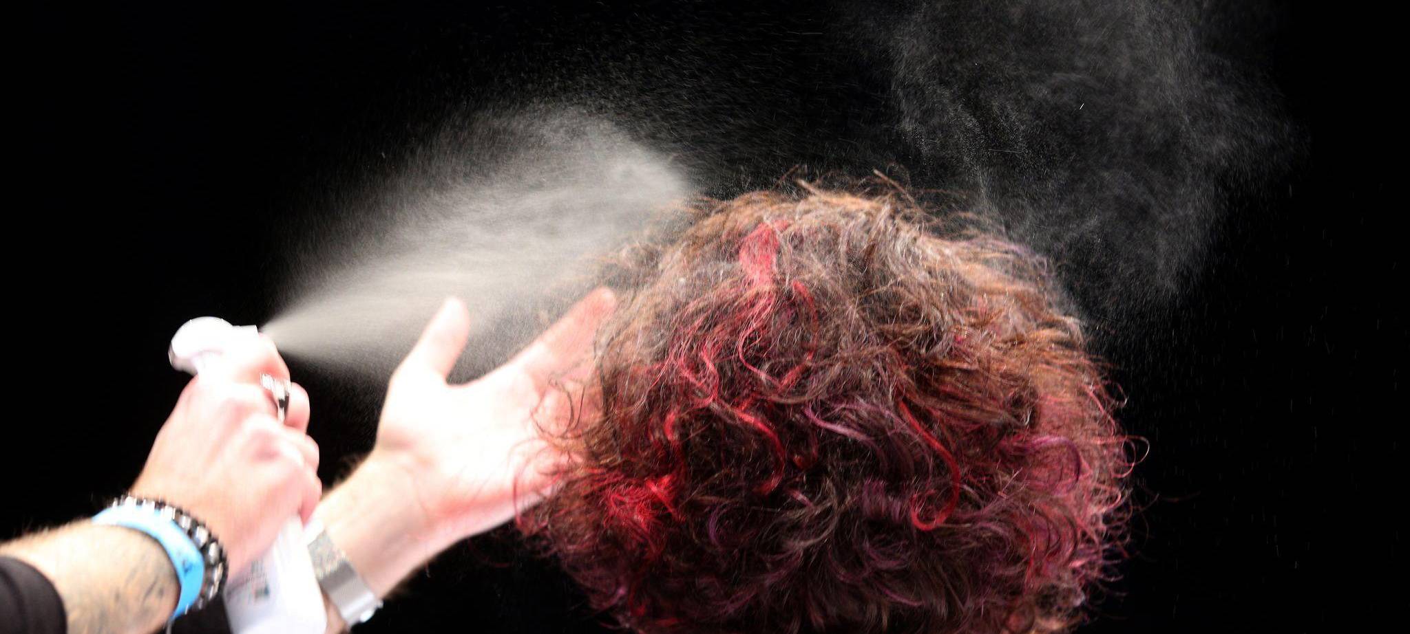 Ein Friseur sprüht einer Frau die Haare mit Haarspray ein